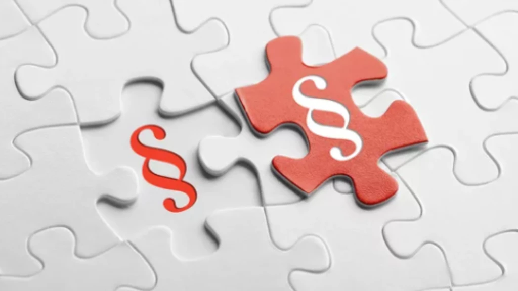 Mehrere ineinander gesteckte weisse Puzzleteile und ein losgelöstes rotes Puzzlestück mit abgebildetem Paragraphen-Symbol.