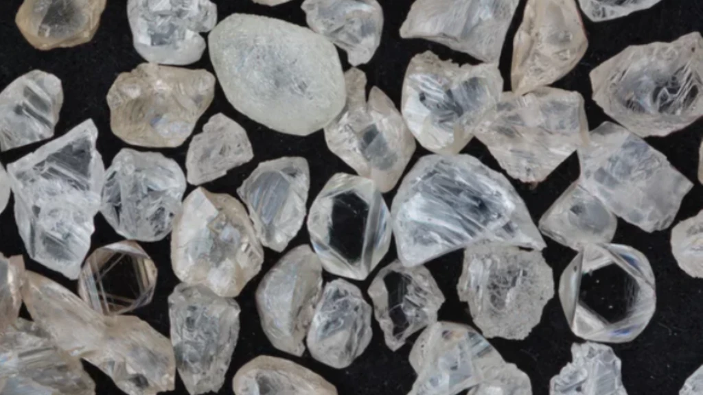 Plusieurs diamants bruts de tailles, formes et nuances de couleur variées sur fond noir.