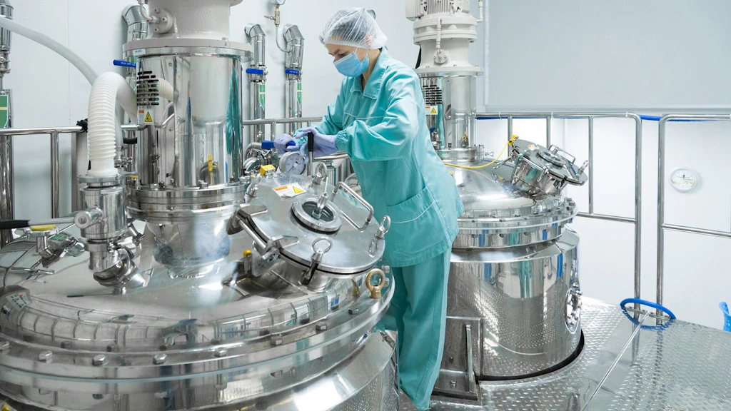 Arbeiterin in einer pharmazeutischen Fabrik in Schutzkleidung, die eine Produktionslinie in einer sterilen Umgebung bedient