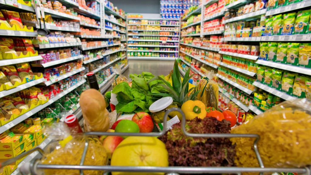 A shopping trolley is standing in an aisle of a supermarket between the shelves.