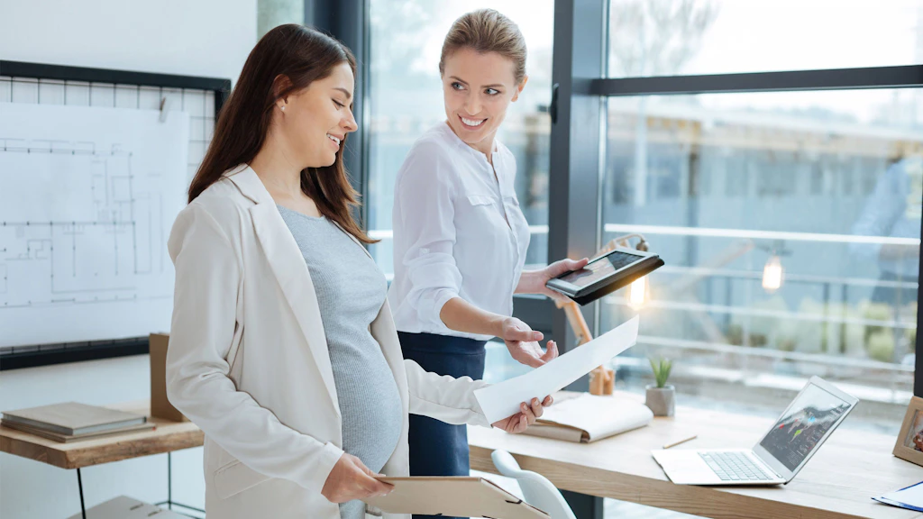Deux femmes sont debout dans un bureau et discutent d'une lettre. L'une d'elles est enceinte.