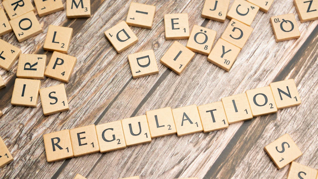 Lose Holzbuchstaben auf einem Tisch; im Vordergrund ist das Wort ‚Regulation‘ gelegt.