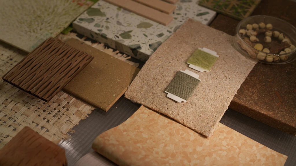 Materialmuster in Naturtönen auf einem Tisch: Platten aus Holz, Stein und Verbundstoffen, daneben kleine Textilproben  sowie eine Schale mit Samen.