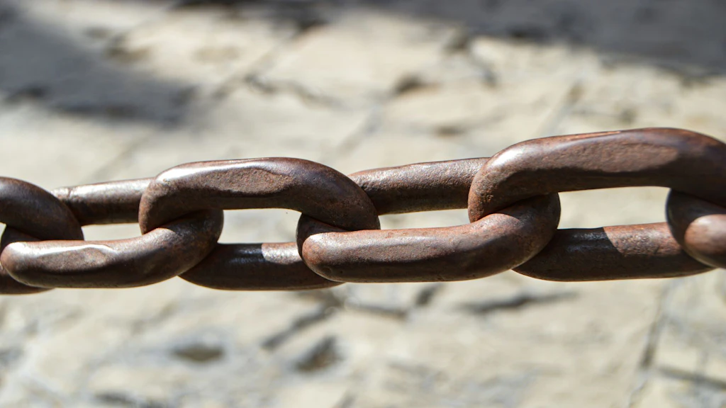 Close-up of a rusty chain over a floor of cobblestones (blurred background).