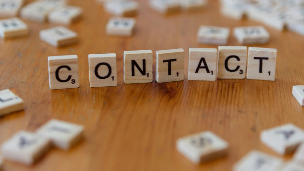 Upright wooden letter tiles form the word "Kontakt" (contact). Other wooden tiles are scattered around it.