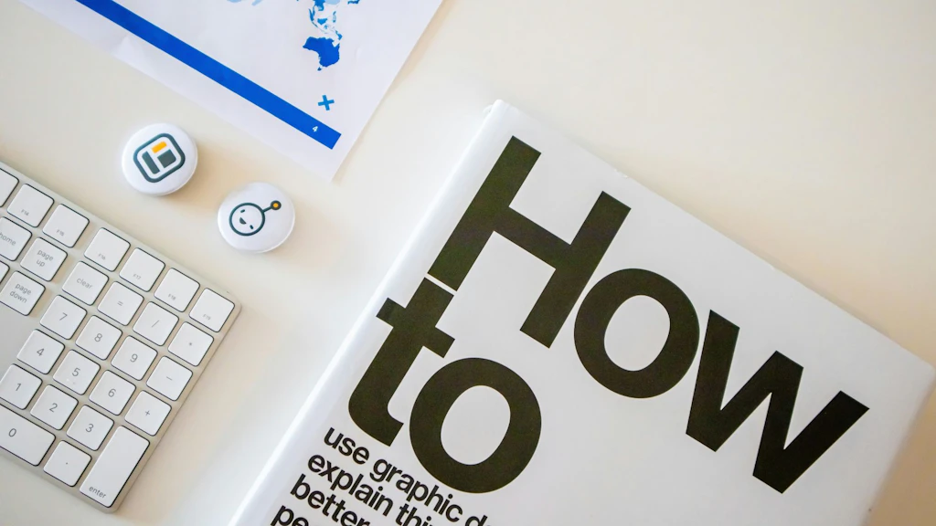 A desk photographed at an angle, featuring a keyboard, a brochure with the words “How to” and graphic symbols, and documents—symbolizing instructions, information, and workflows.