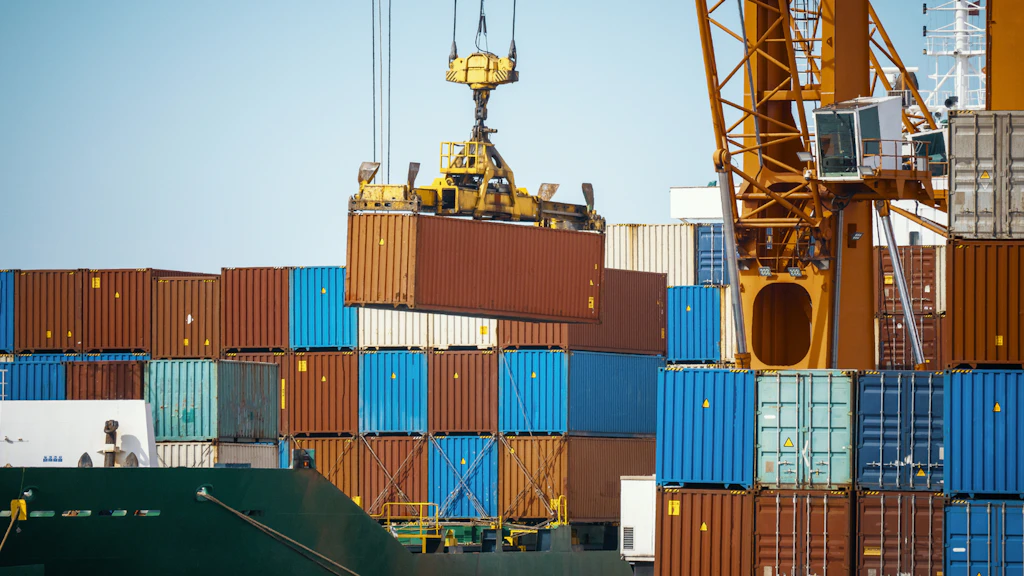 Ein Frachtcontainer wird gerade von einem Hafenkran über einen Stapel bunter Container gehoben