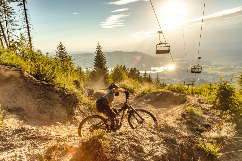 Eine Person die auf einem Mountenbike unter einer Sesselbahn den Berg herunterfährt.