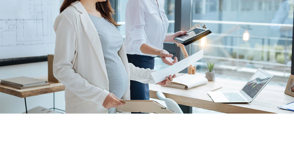 Zwei Frauen stehen im Büro und besprechen einen Brief. Eine Frau ist schwanger.