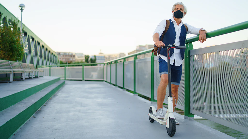 Mann mit Atemmaske steht mit einem Trottinett auf einer Brücke