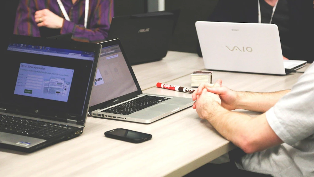 Drei Personen mit ihren Laptops sitzen um einen Tisch und diskutieren.