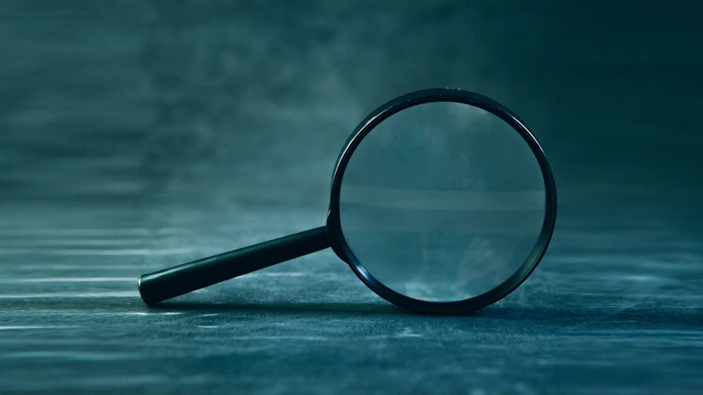 A black magnifying glass stands on its edge against a dark background.