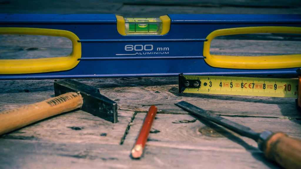 Tools such as a level, a tape measure, and a pencil are laid out on a wooden surface, symbolizing the fundamentals and instruments of accreditation
