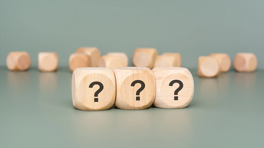 Des cubes en bois sur fond vert, dont trois portent un point d'interrogation.