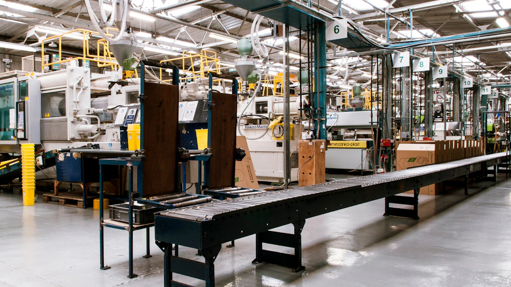 Une chaîne de production industrielle dans une usine, avec un convoyeur au premier plan et des machines automatisées, structures métalliques et équipements techniques disposés tout autour
