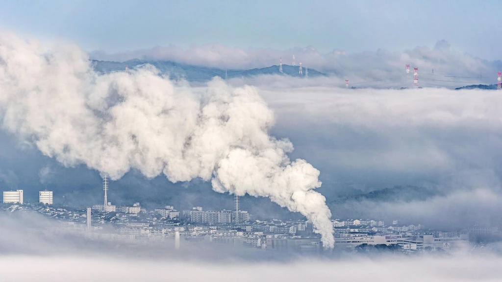 Depuis les hauteurs, on aperçoit une ville enveloppée de nuages et de smog.