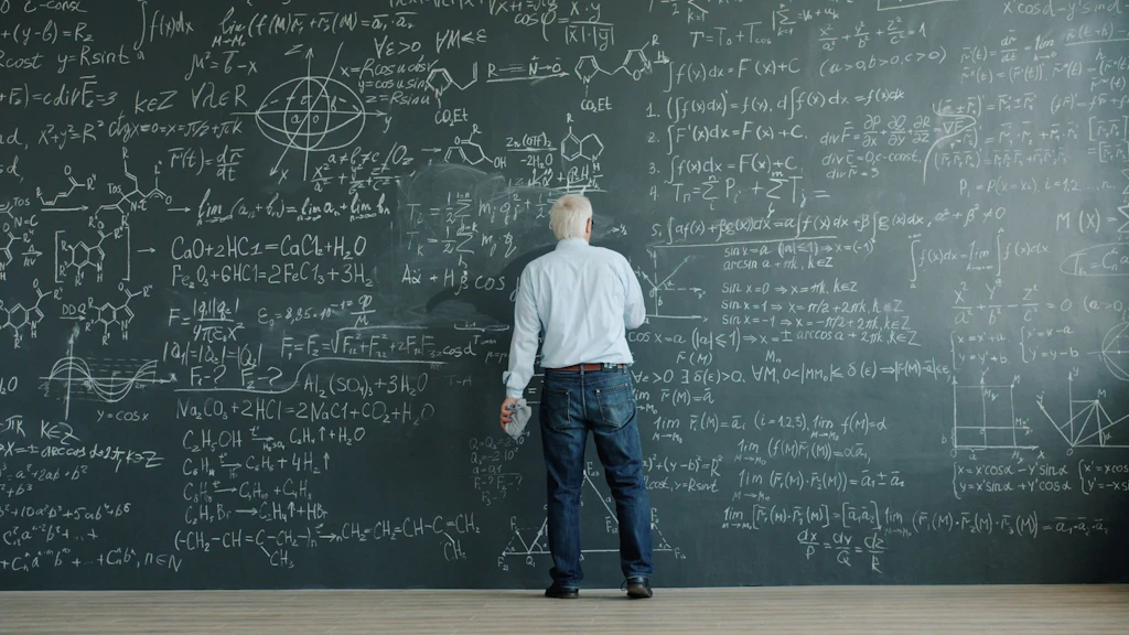 Un homme, dos à la caméra, écrit sur un grand tableau couvert de formules