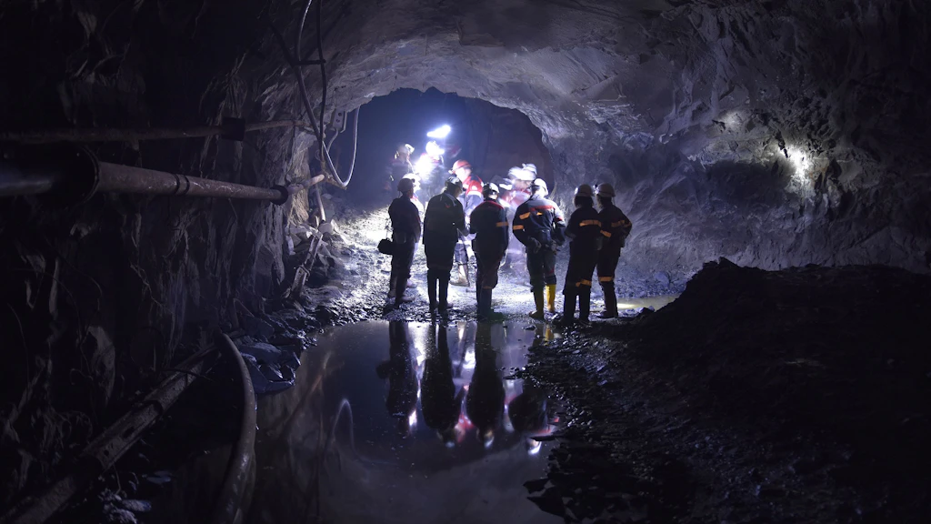 Plusieurs travailleurs de tunnel se tiennent dans une galerie sombre avec des casques et des lampes frontales, la lumière se reflétant sur le sol mouillé.
