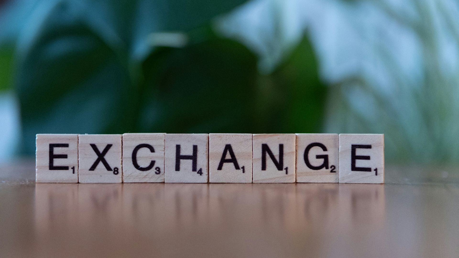 Huit cubes de lettres disposés sur une table forment le mot «EXCHANGE». L'arrière-plan est flou et de couleur verte. L'image symbolise l'échange avec les parties prenantes.