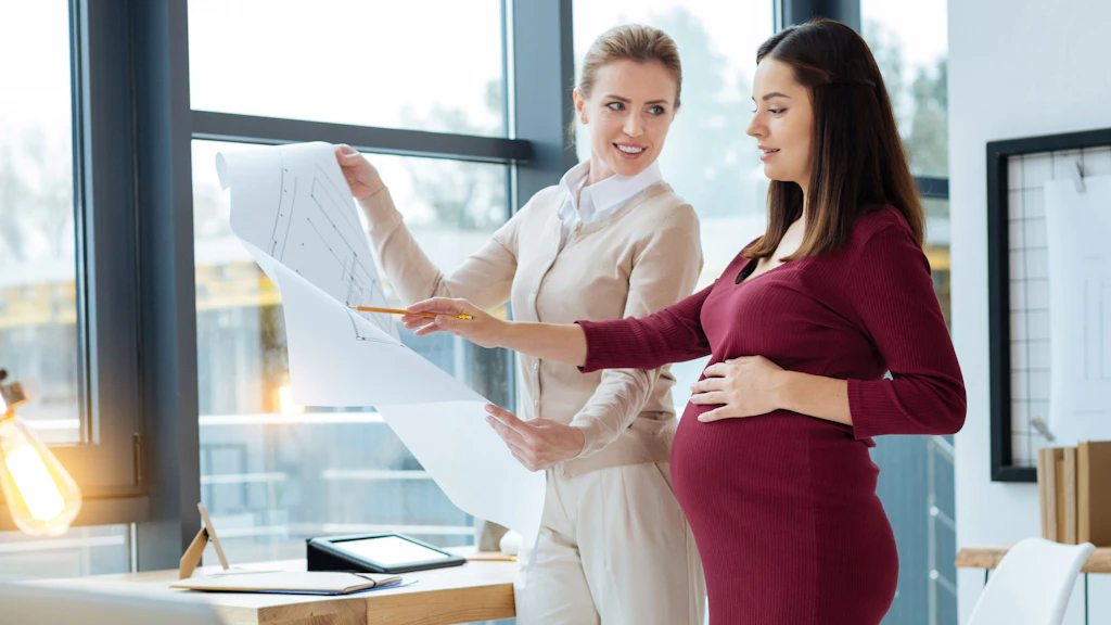 Deux femmes sont debout dans un bureau et discutent d'un plan de construction. L'une d'elles est enceinte.