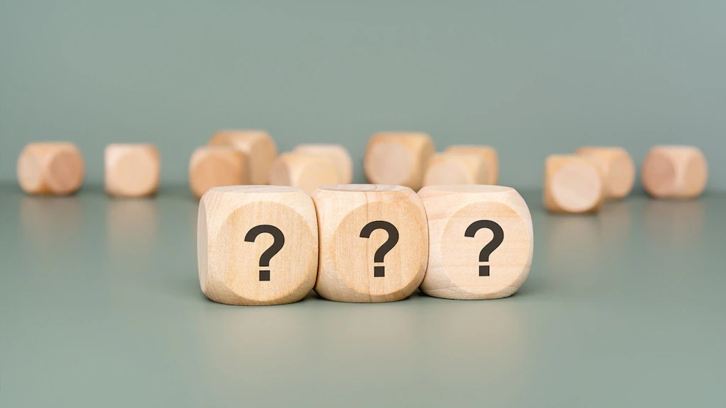 Cubetti di legno su sfondo verde, con un punto interrogativo su tre di essi.