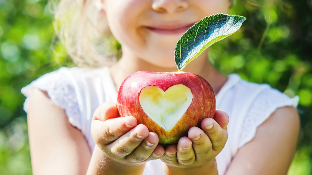 Un bambino tiene tra le mani una mela con un cuore inciso