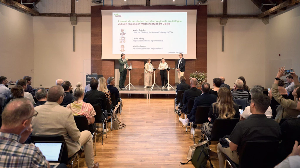 Una sala conferenze con il pubblico seduto di fronte a un palco dove quattro persone stanno partecipando a una discussione.